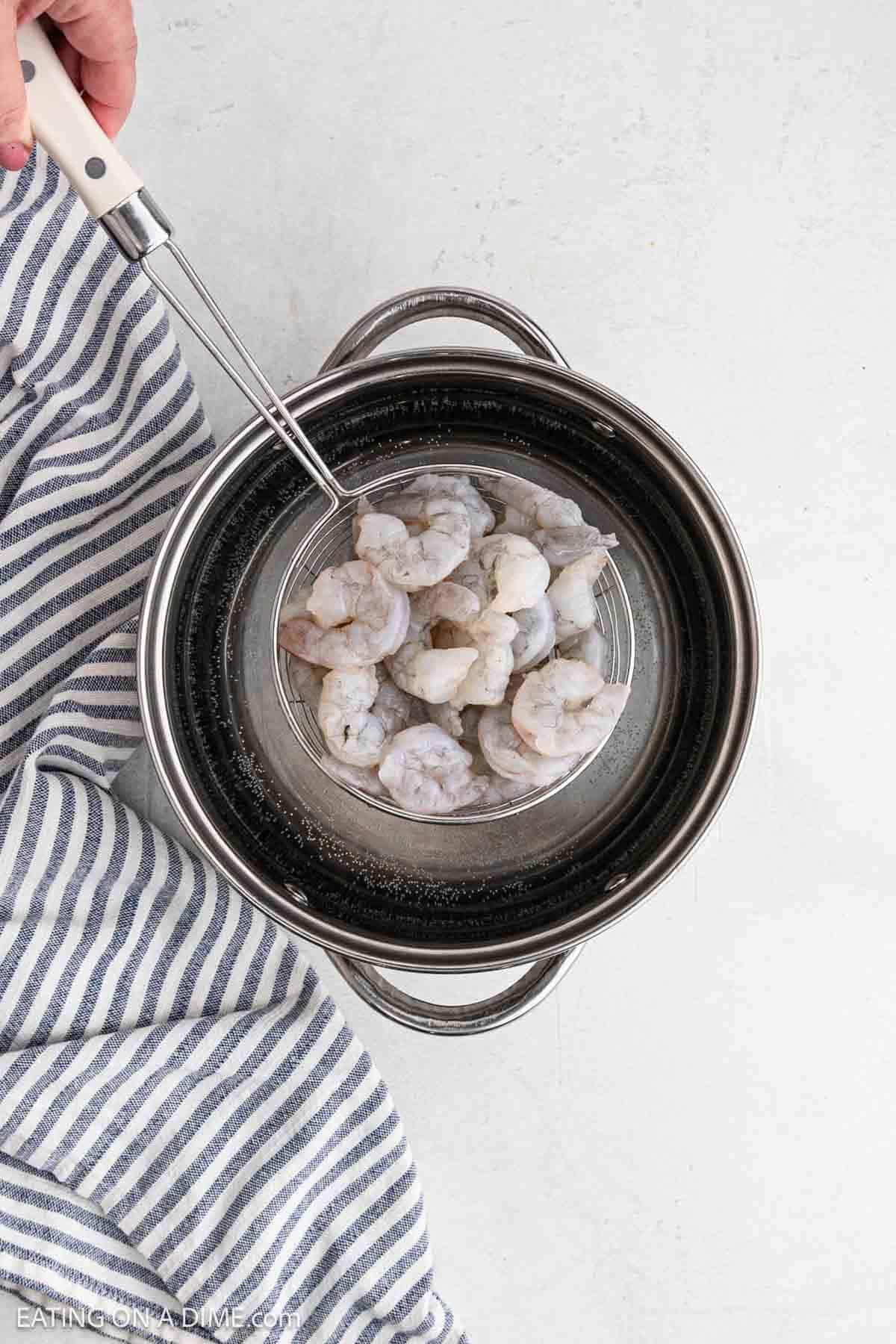 Raw shrimp in a colander over a large pot of water.