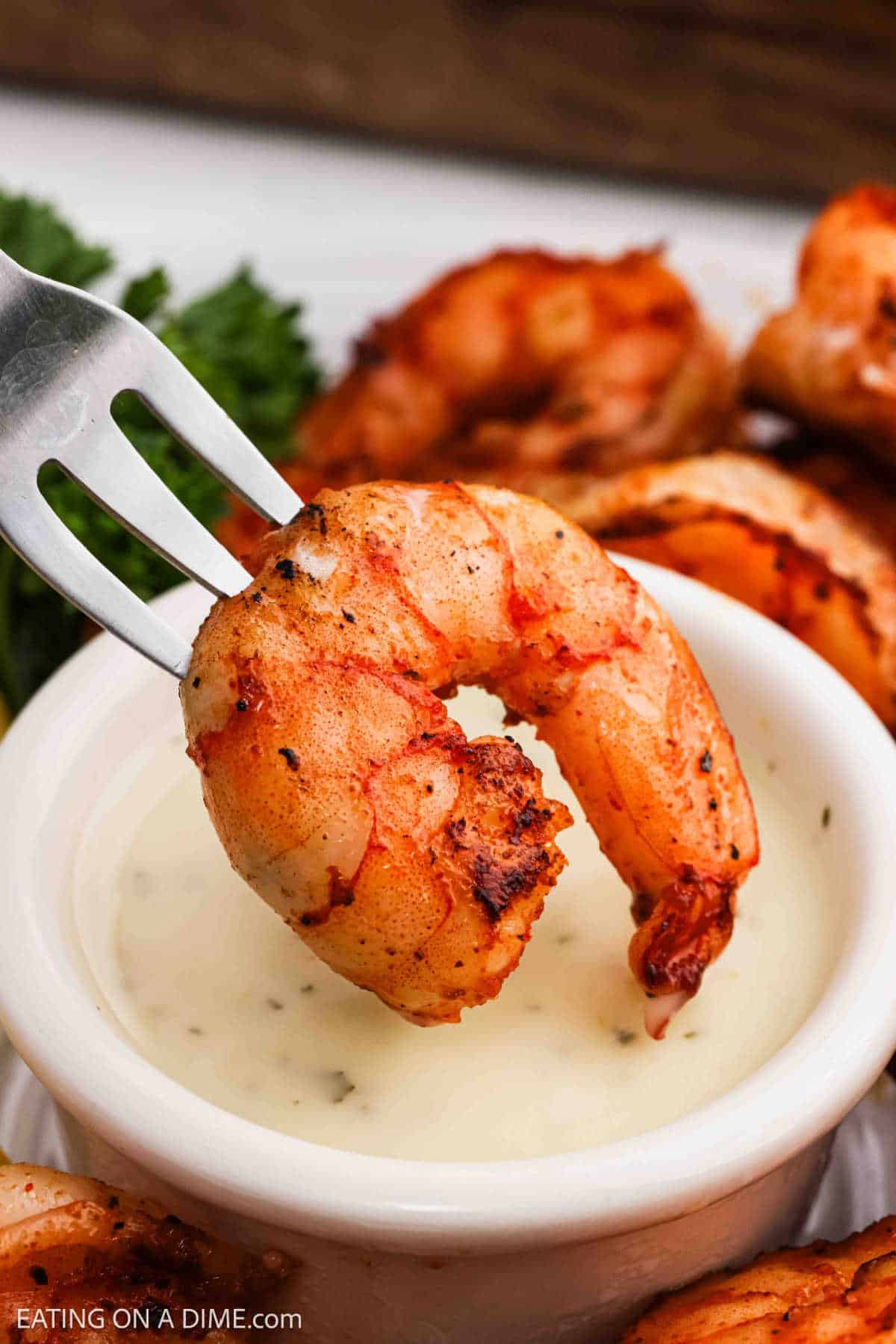 Close up image of blackened shrimp on a fork being dipped into sauce.