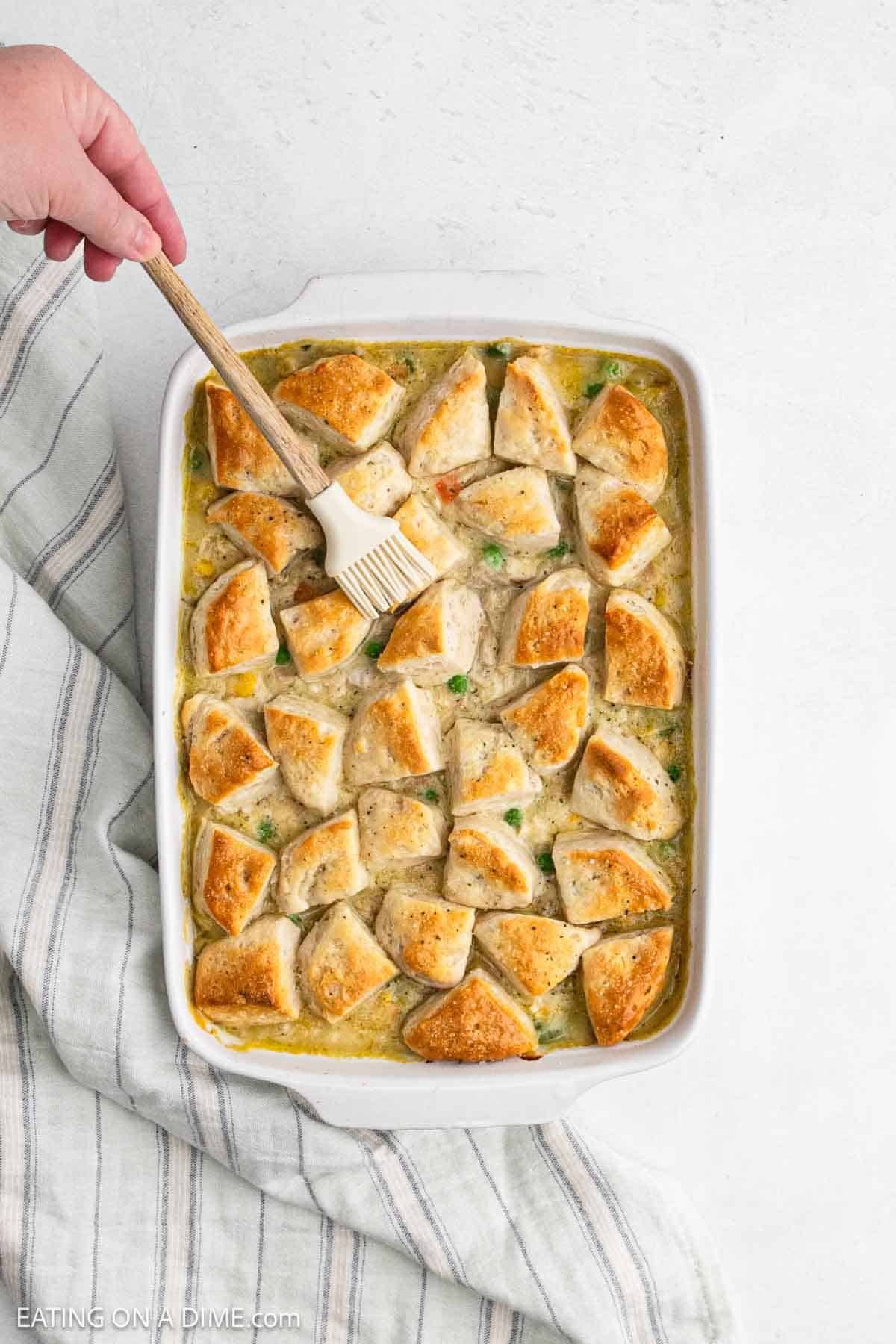 Brushing melted butter over the baked casserole.