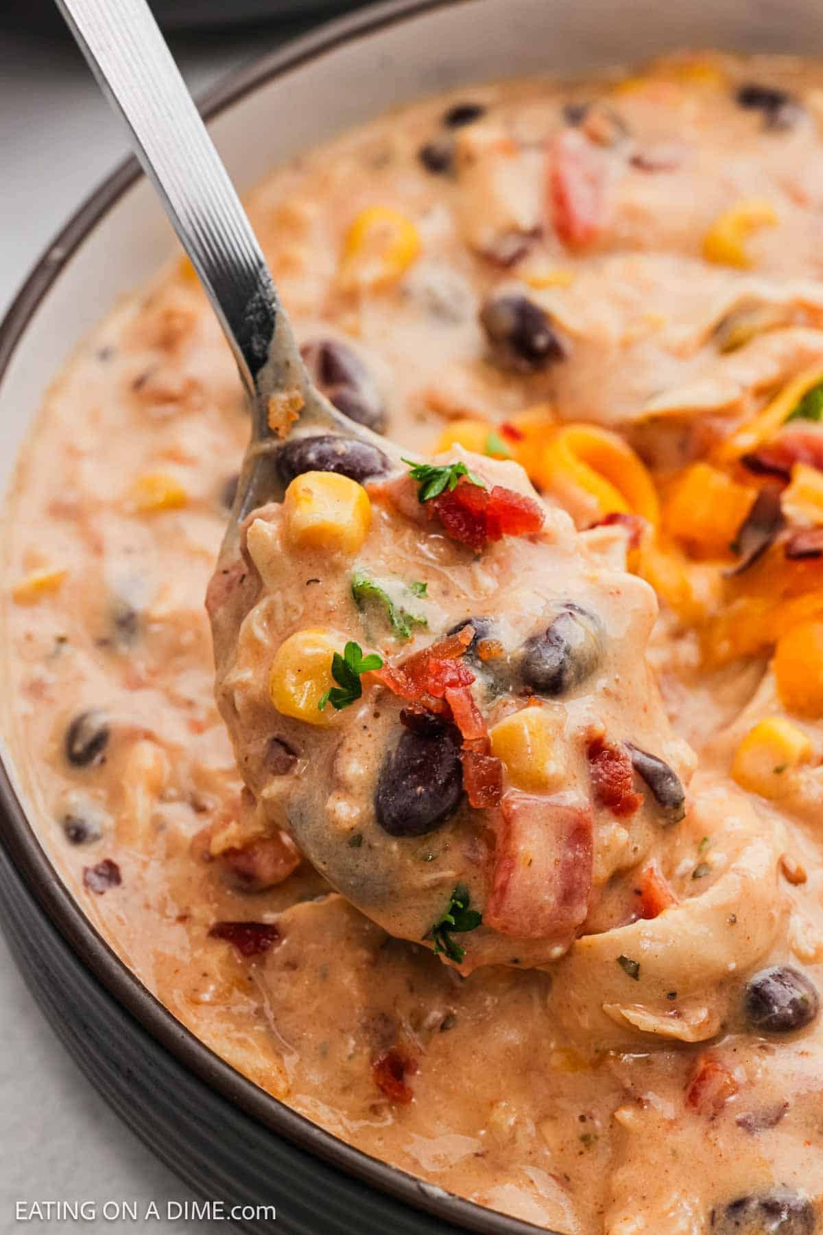 Creamy chicken chili in a bowl with a bite on a spoon.