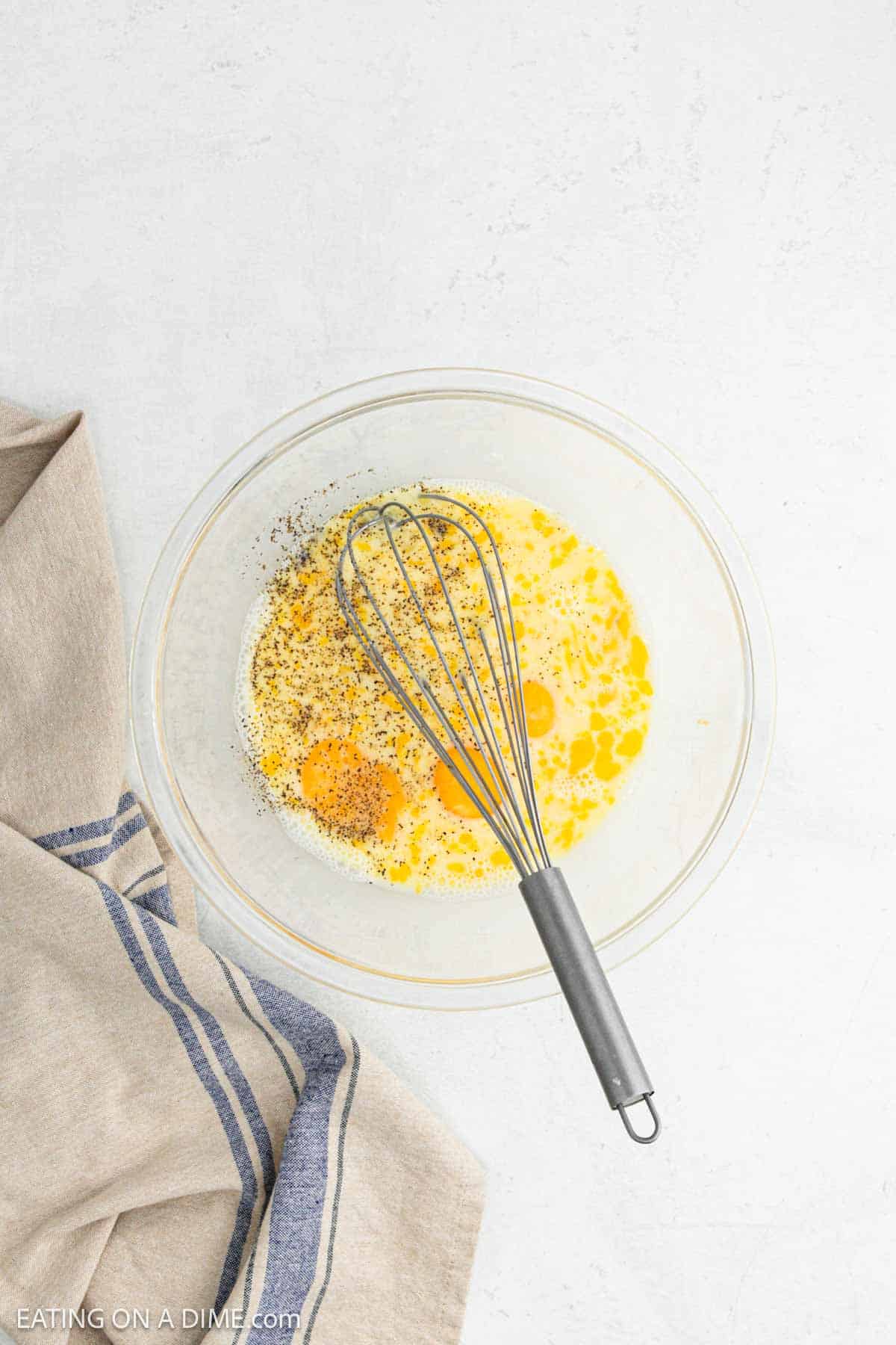 Mixing whole eggs and spices together in a bowl with a whisk.