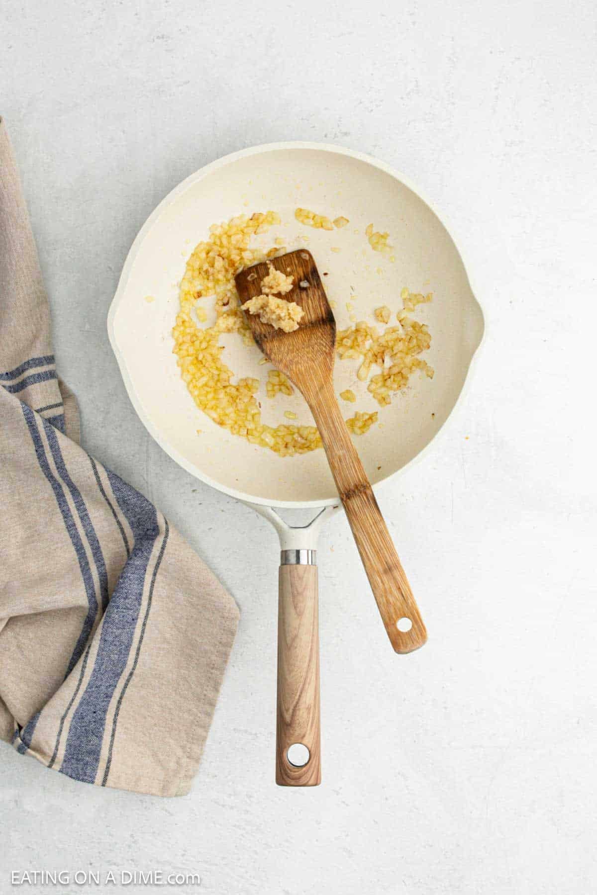 Sauteed onions in a skillet with minced garlic on the wooden spoon.