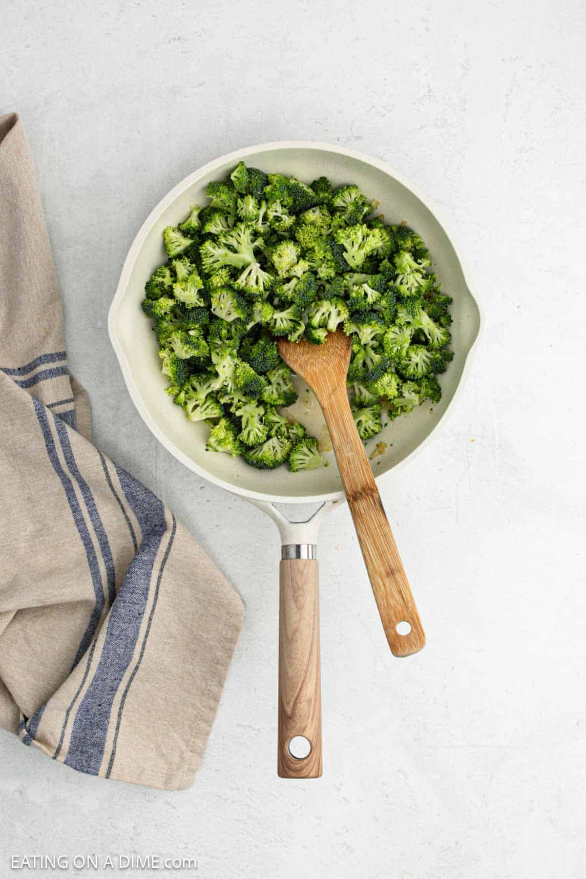 Chopped broccoli in a skillet with a wooden spoon.