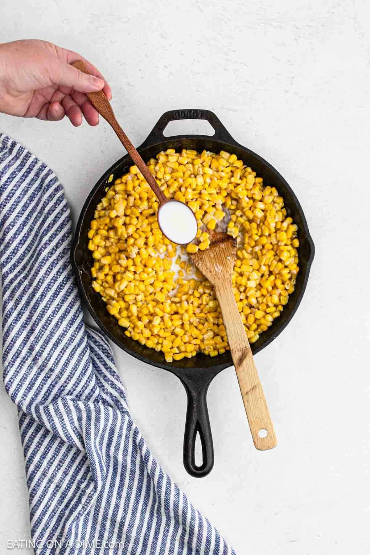 Adding a tablespoon of milk to the corn mixture in a cast iron skillet.