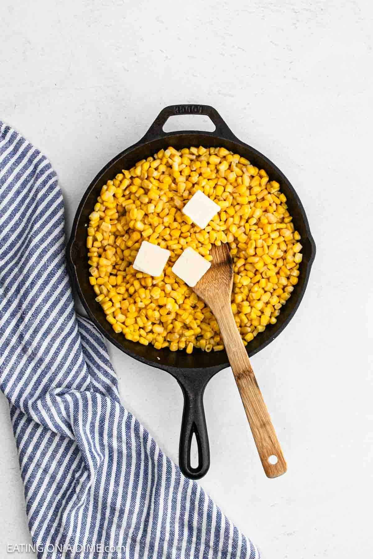 Butter slices topped corn kernels in a cast iron skillet.