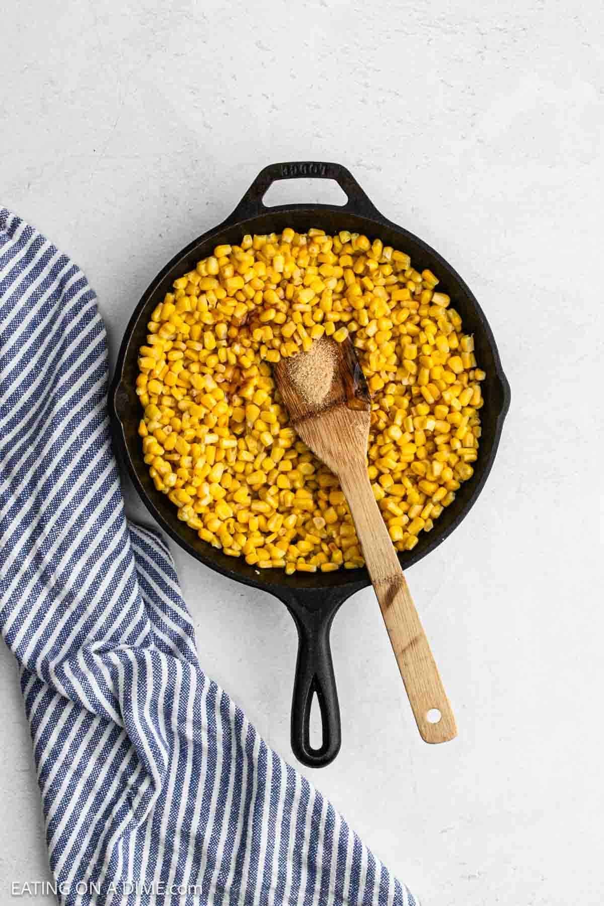 Adding spices and honey to the corn kernels in a cast iron skillet.