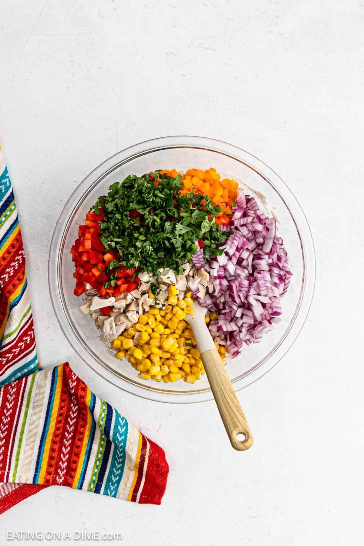 Cilantro, red onions, corn, bell peppers, and cooked in a bowl with a wooden spoon.