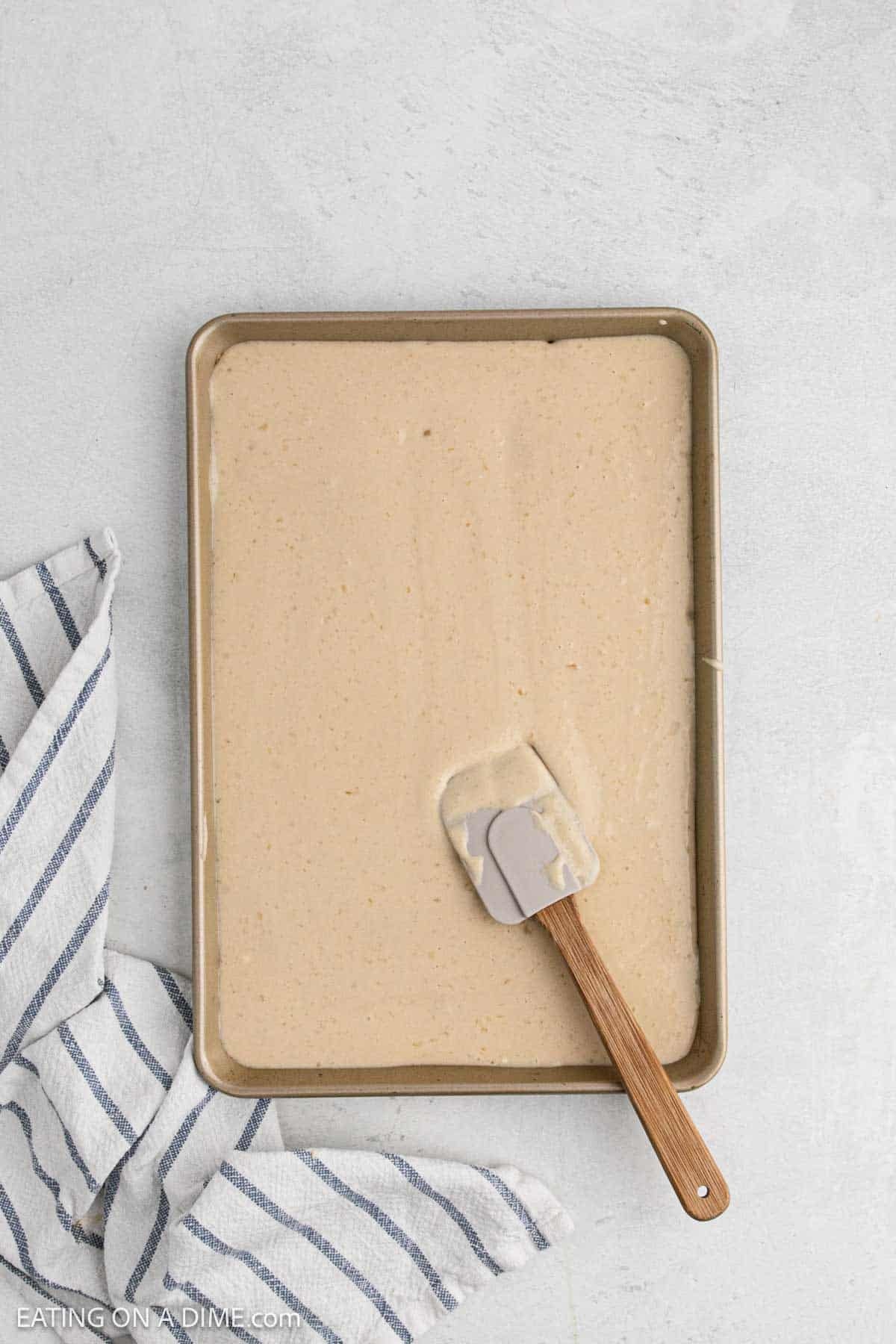Spreading the pancake batter in a baking sheet with a spatula.