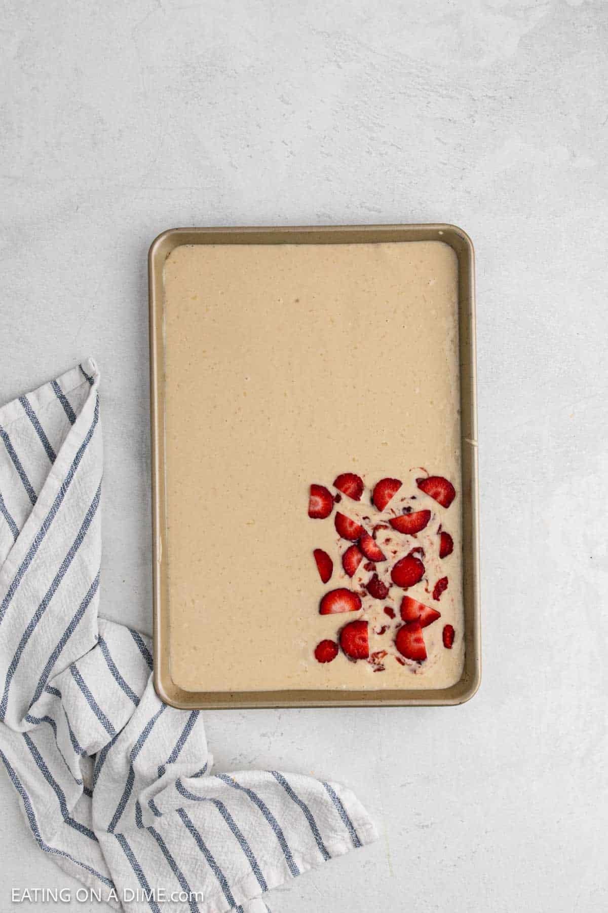 Topping the batter with strawberries in one corner of the pan.