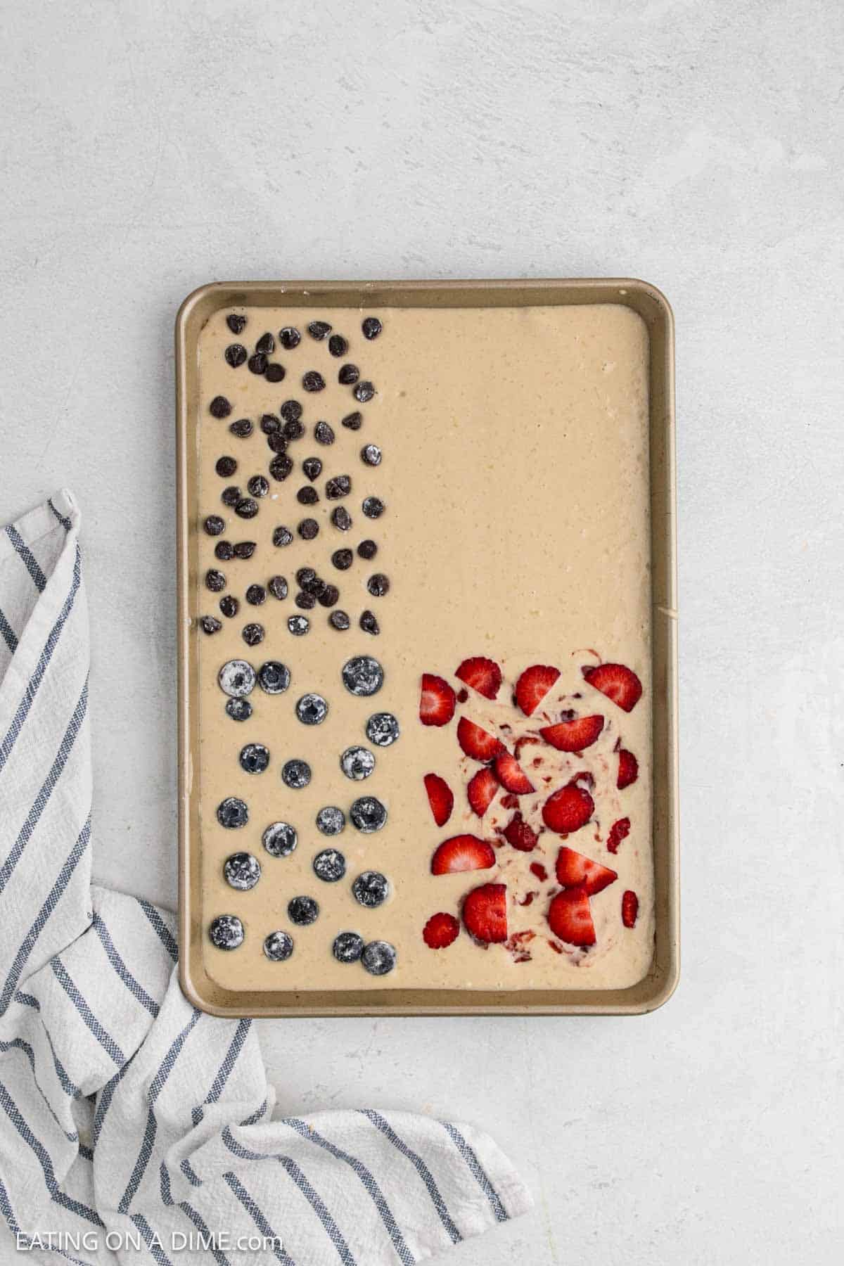 Topping the batter with strawberries, blueberries, and chocolate chip in the pan.