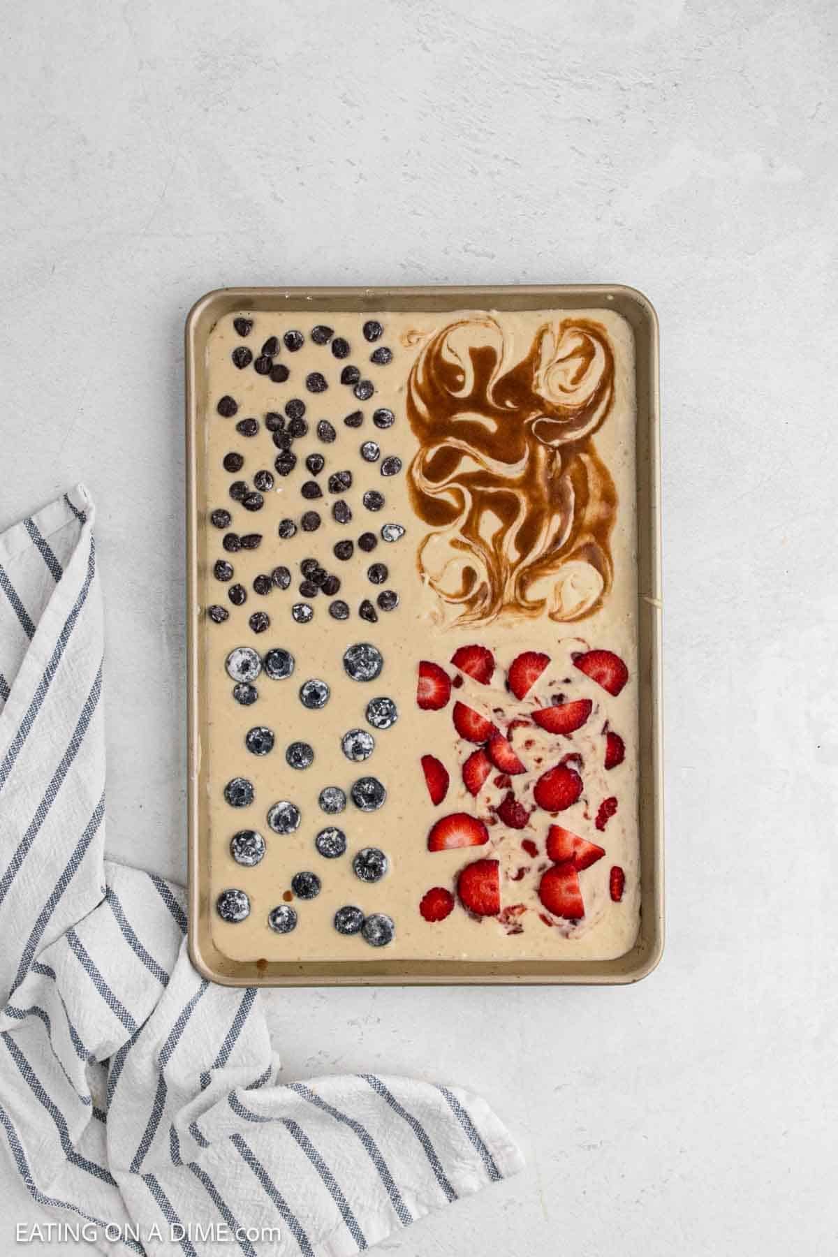 Topping the batter with strawberries, blueberries, chocolate and cinnamon swirl in a pan.