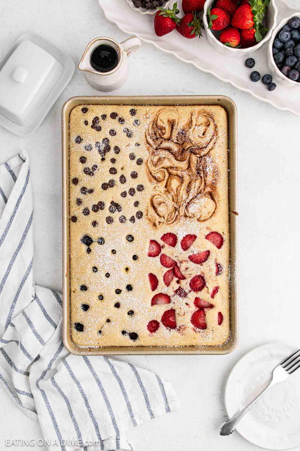 Baked pancakes in a pan topped with strawberries, chocolate chips, blueberries and cinnamon swirl.