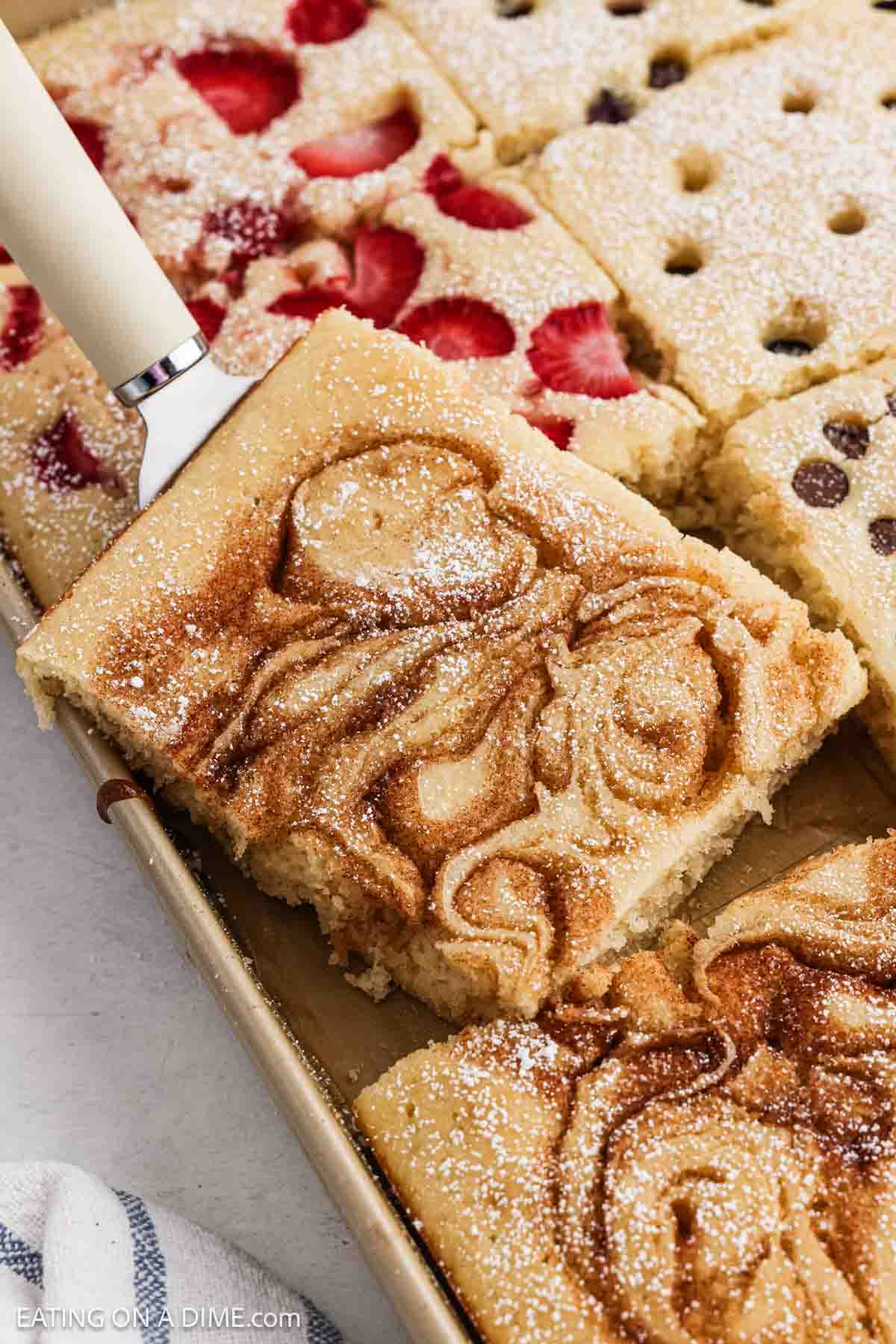 Baked pancakes in a pan topped with cinnamon, strawberries, and chocolate chips.