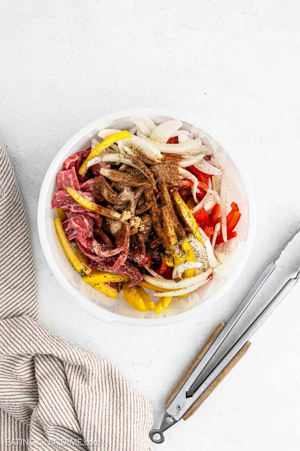 Steak stips and bell peppers in a bowl topped with spices.