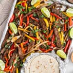 Steak Fajitas on a foil lined baking sheet with a side of tortillas.