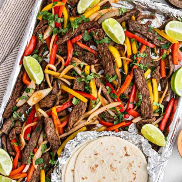 Steak Fajitas on a foil lined baking sheet with a side of tortillas.