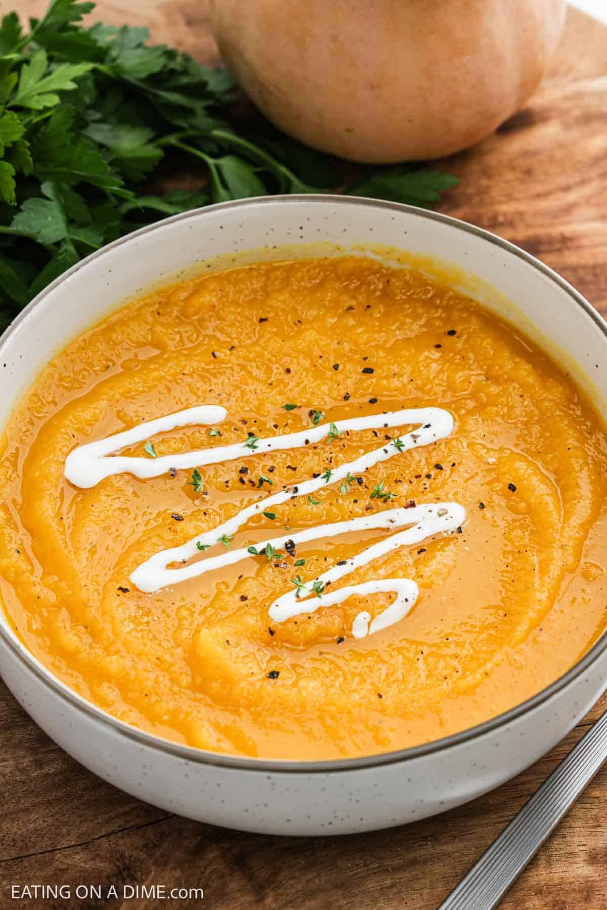 Blended soup in a bowl topped with fresh herbs and a drizzle of heavy cream.