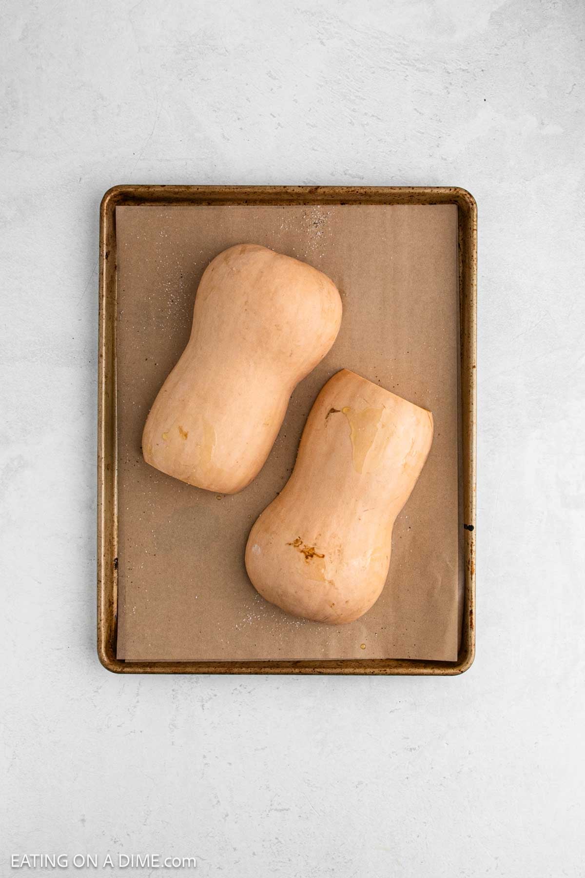 Butternut squash cut in half on a baking sheet lined with parchment paper.