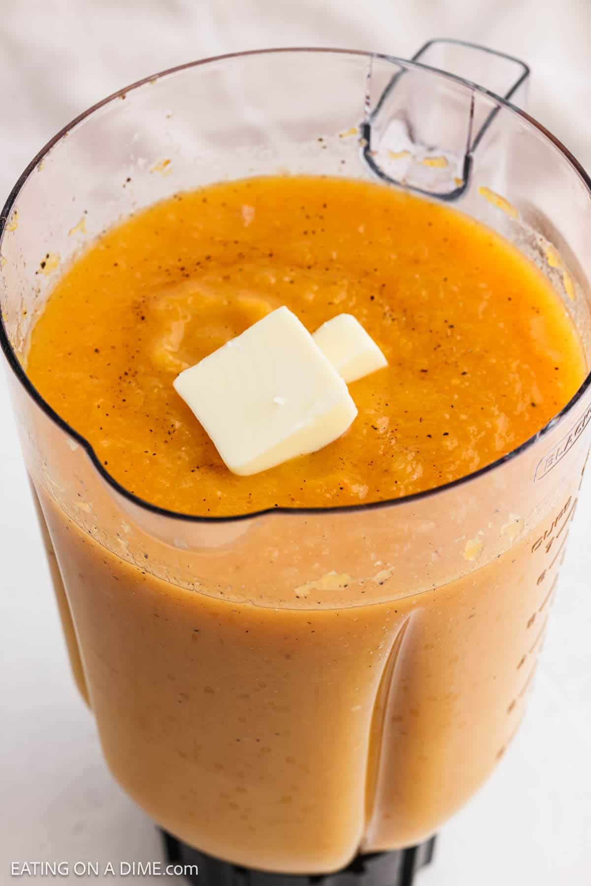 Blended soup in the blender topped with a slice of butter.