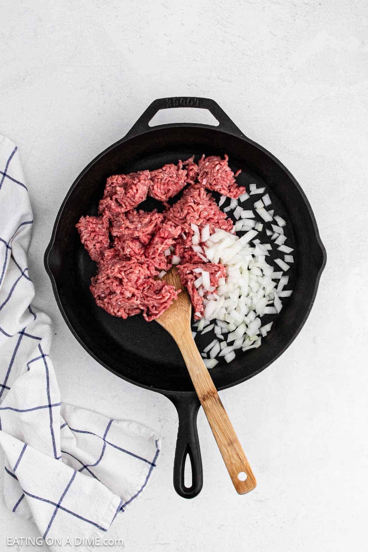 Cooking ground beef in a cast iron skillet with diced onions.