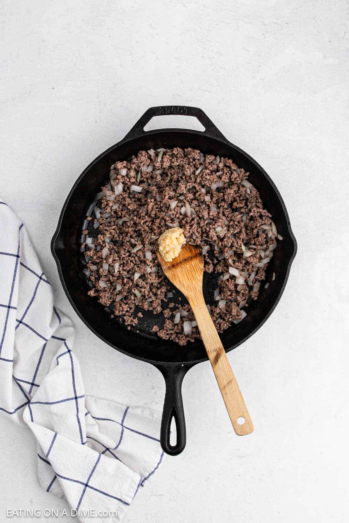 Cooked ground beef with onions and garlic in a cast iron skillet with a wooden spoon.