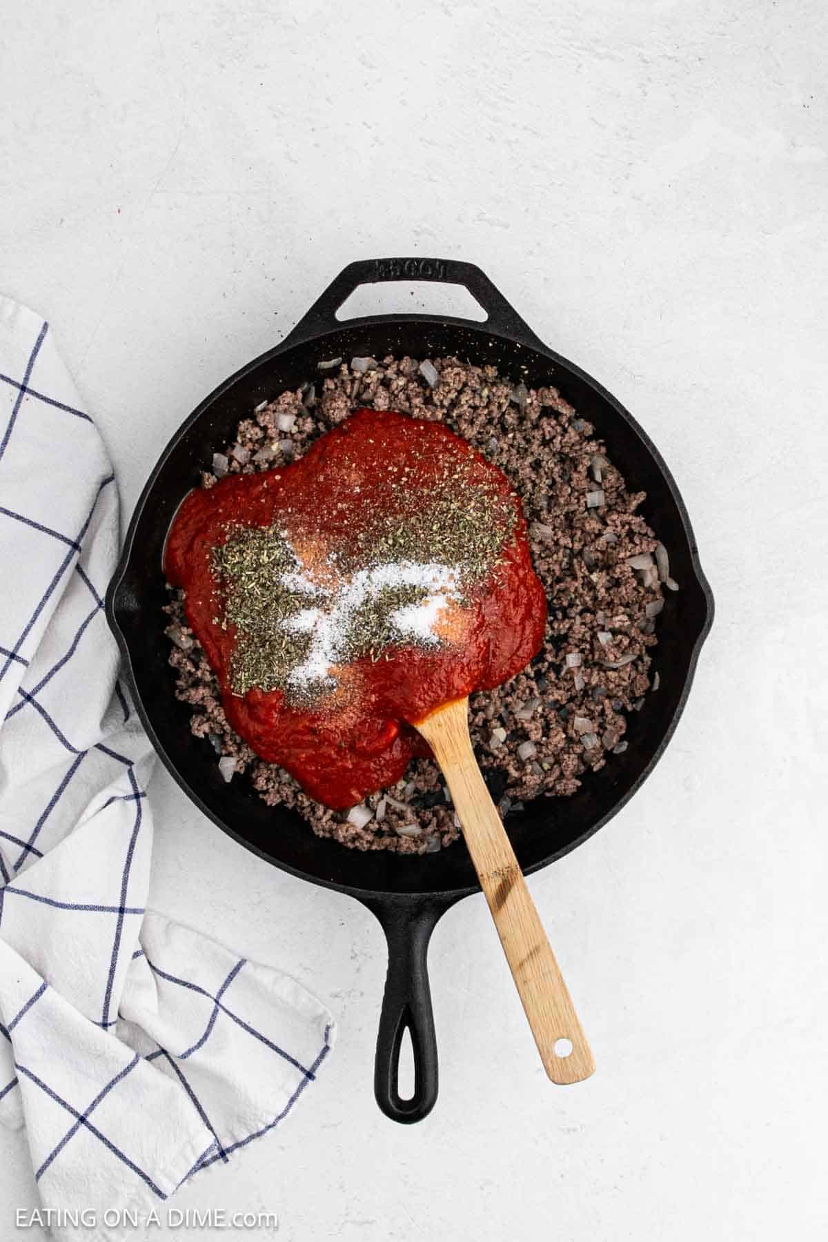 Cooked ground beef in a cast iron skillet topped with marinara sauce and spices.