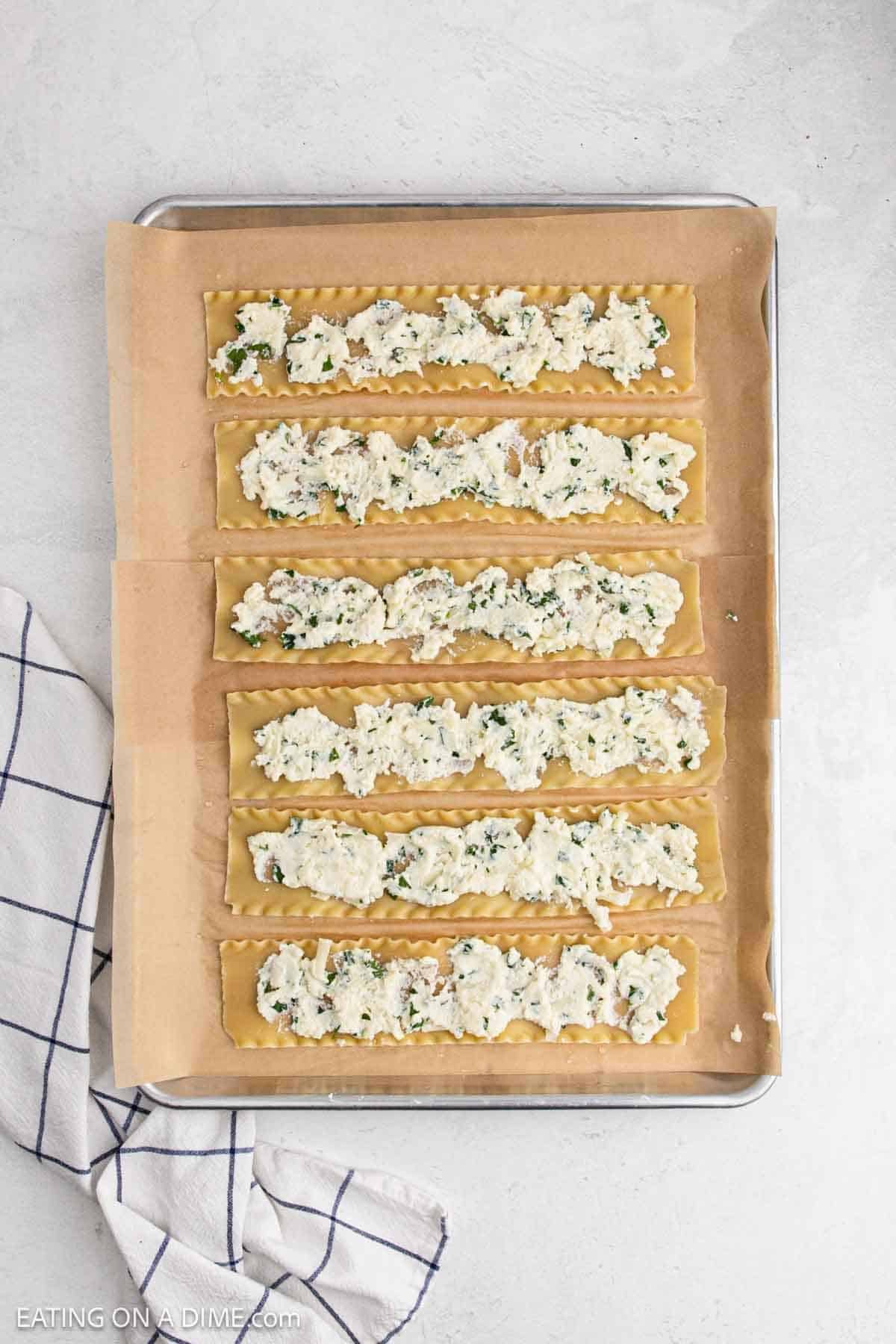 Cooked lasagna noodles on a baking sheet lined with parchment paper topped with the ricotta mixture.