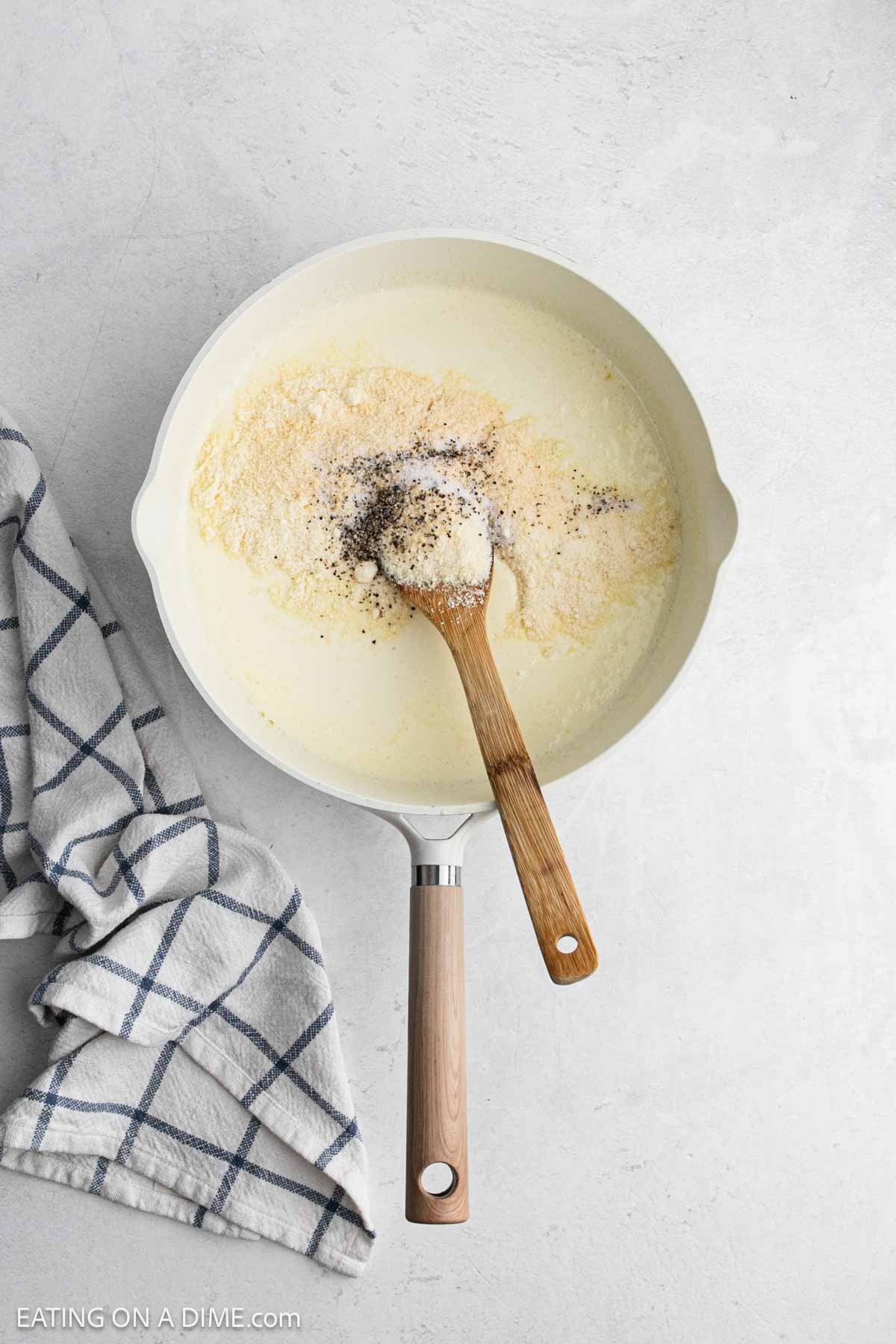 Flour and spices is mixed with a creamy sauce in a skillet with a wooden spoon.