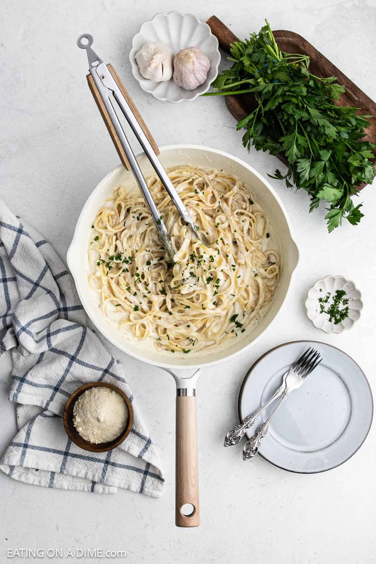 Fettuccine alfredo in a skillet with tongs on top.