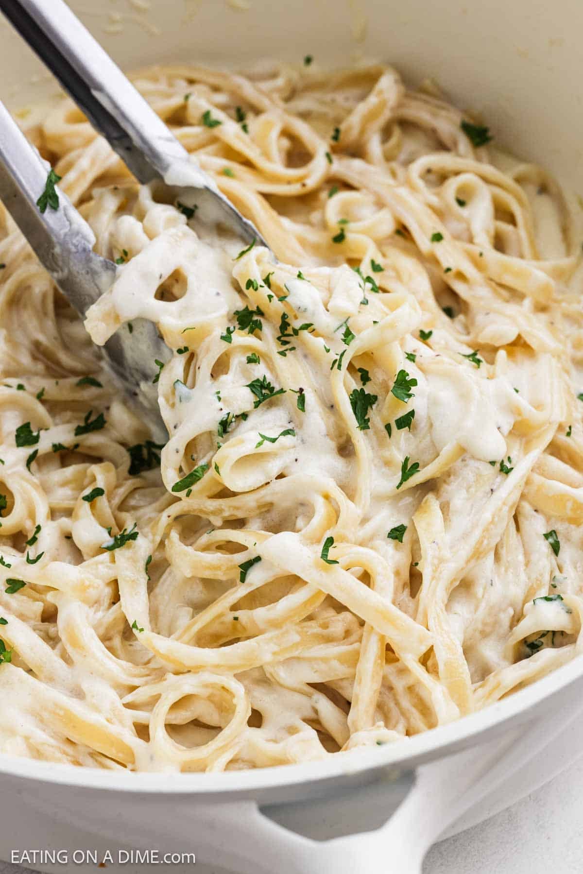 Close up image of fettuccine pasta mixed in a creamy sauce in a skillet.