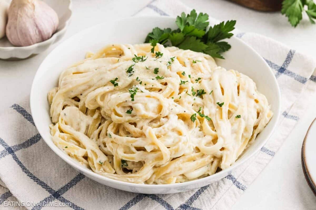 Fettuccine alfredo in a bowl topped with fresh herbs.