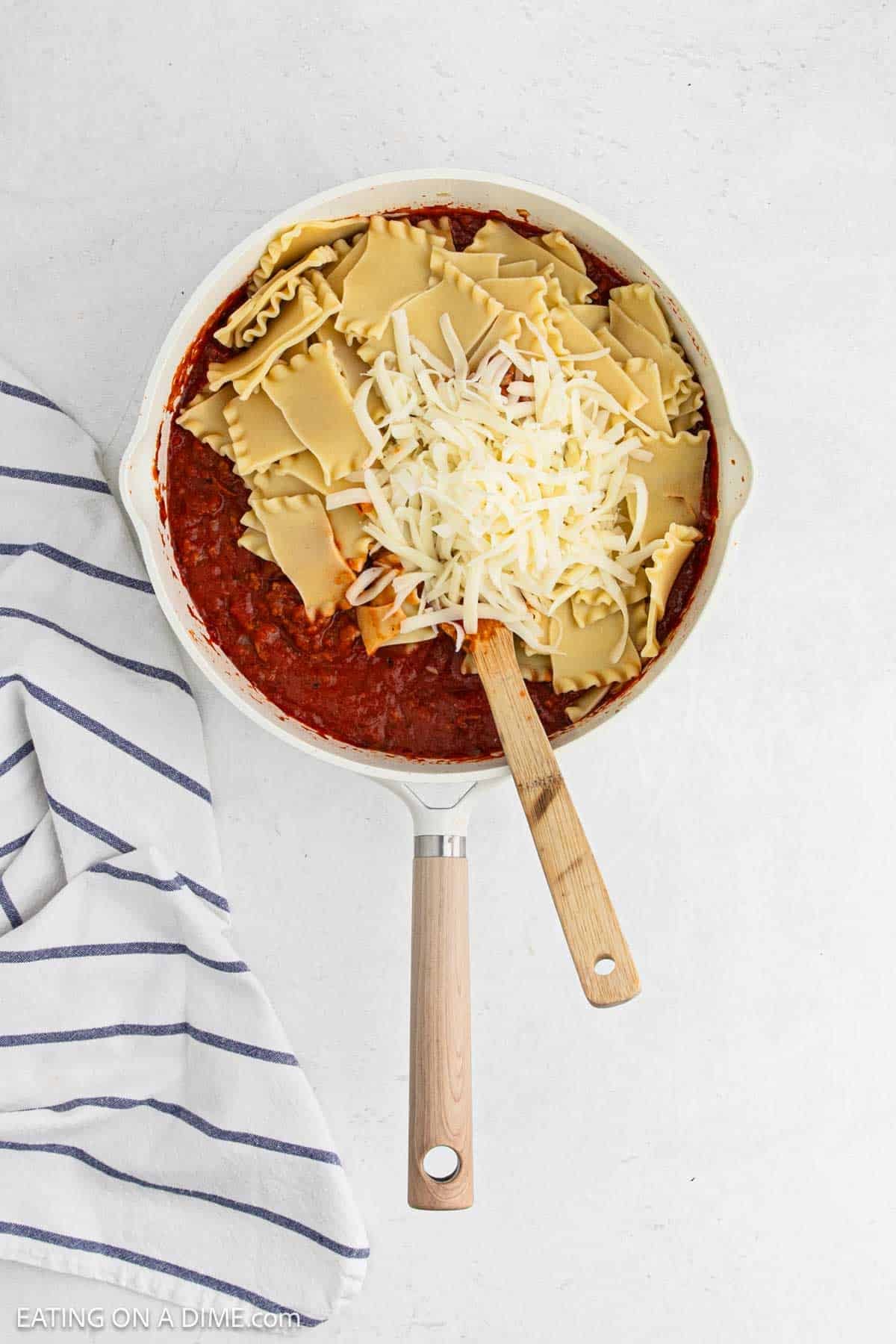 Meat sauce topped with broken cooked lasagna noodle topped with shredded cheese in a skillet.