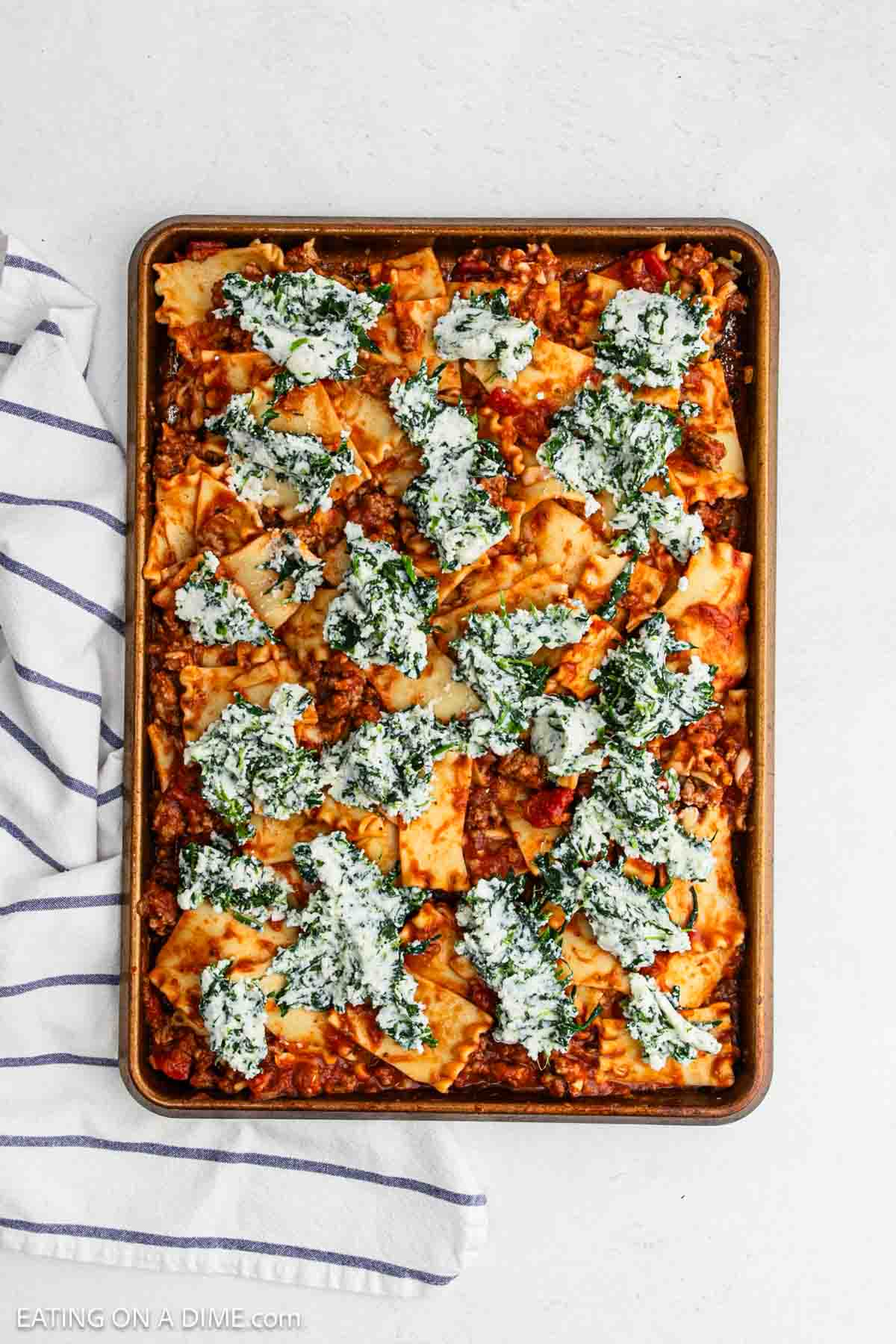 Lasagna and meat sauce spread on a sheet pan topped with spinach ricotta cheese.