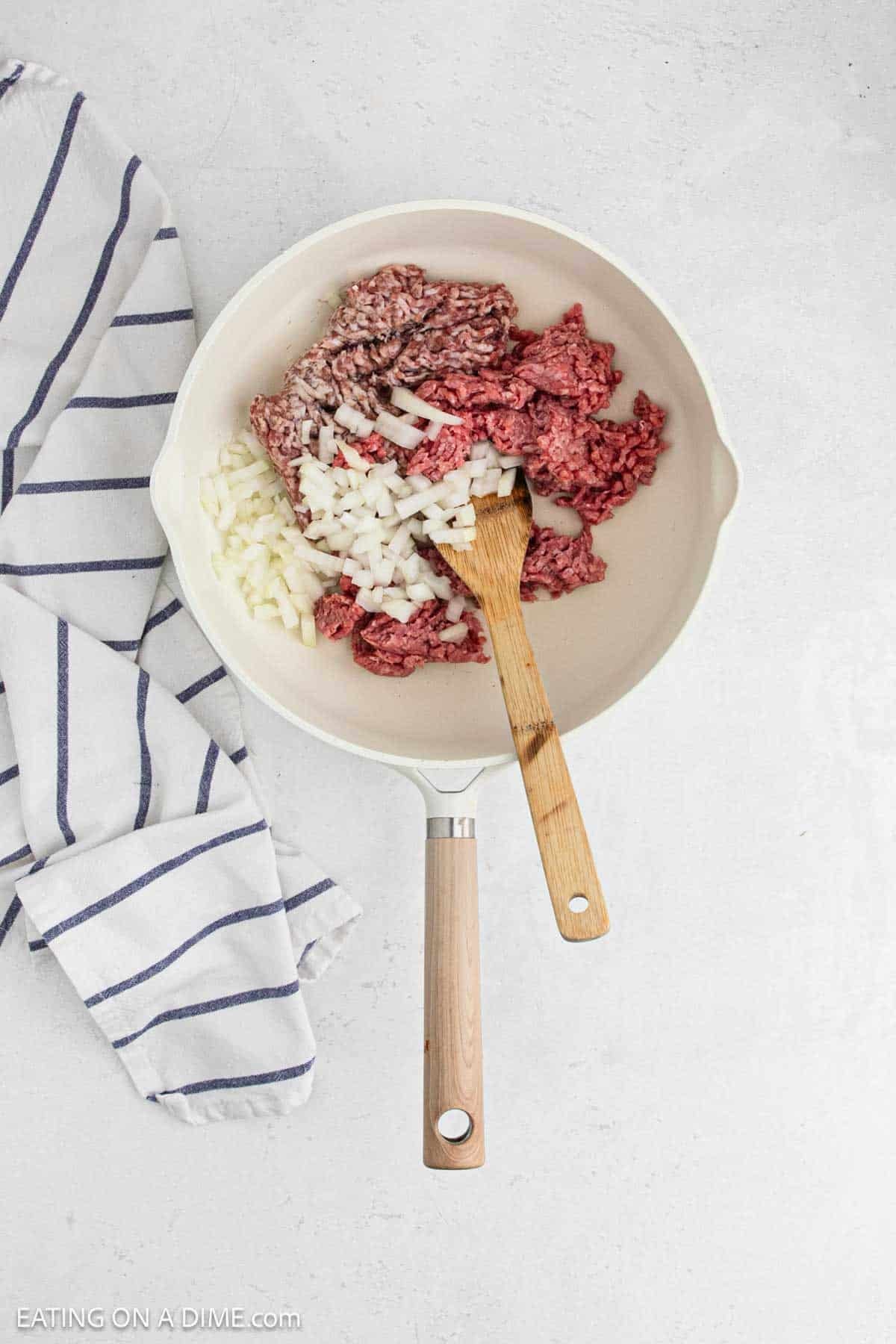 Ground beef, Italian sausage with diced onions in a large skillet with a wooden spoon.