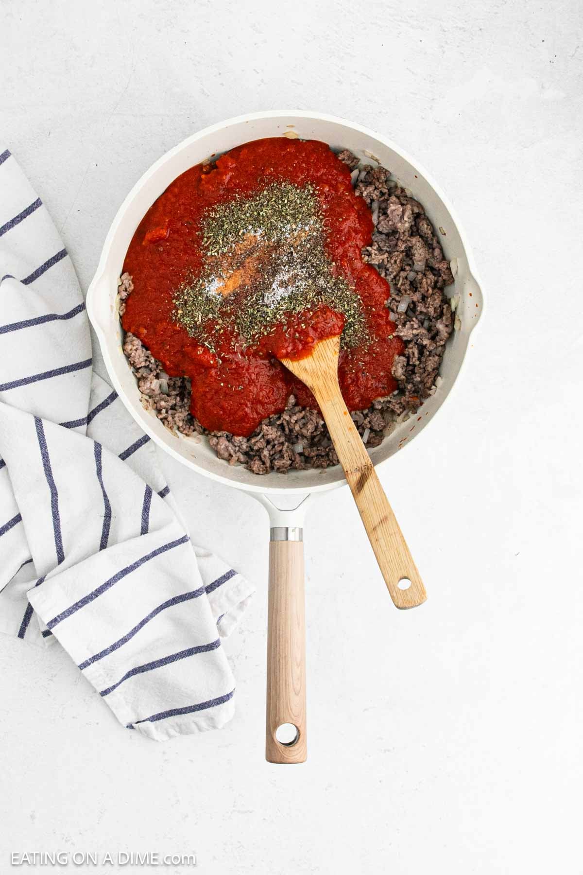 Cooked ground meat topped with tomato sauce and seasoning in a skillet.