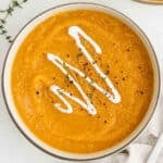 Butternut squash soup in a large pot topped with a drizzle of sour cream.