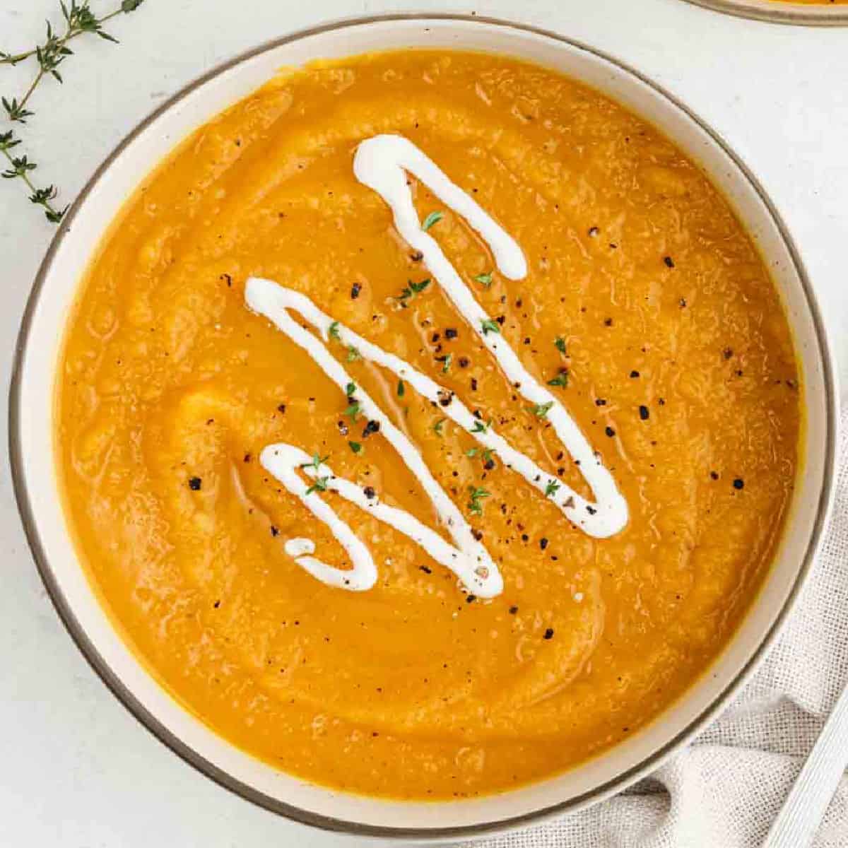 Butternut squash soup in a large pot topped with a drizzle of sour cream.
