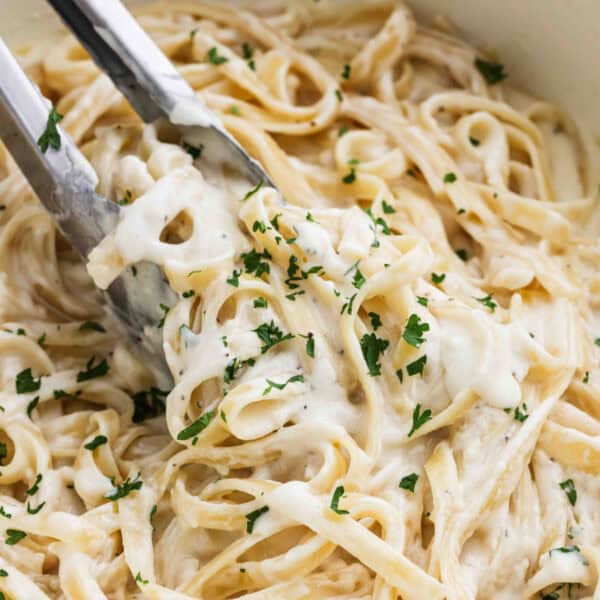 Fettuccine alfredo in a large skillet with a serving in between tongs.