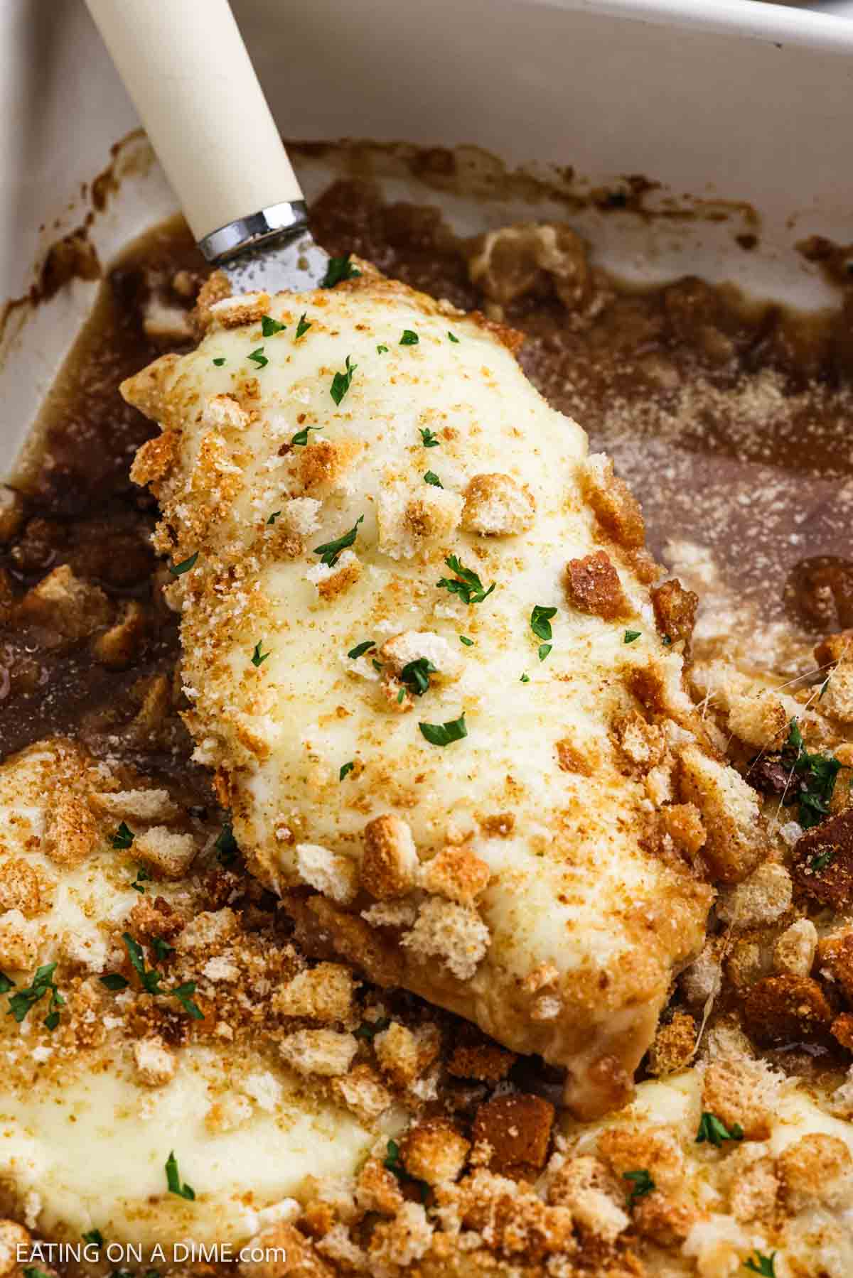 Chicken breast on a spatula topped with melted cheese and crushed croutons.